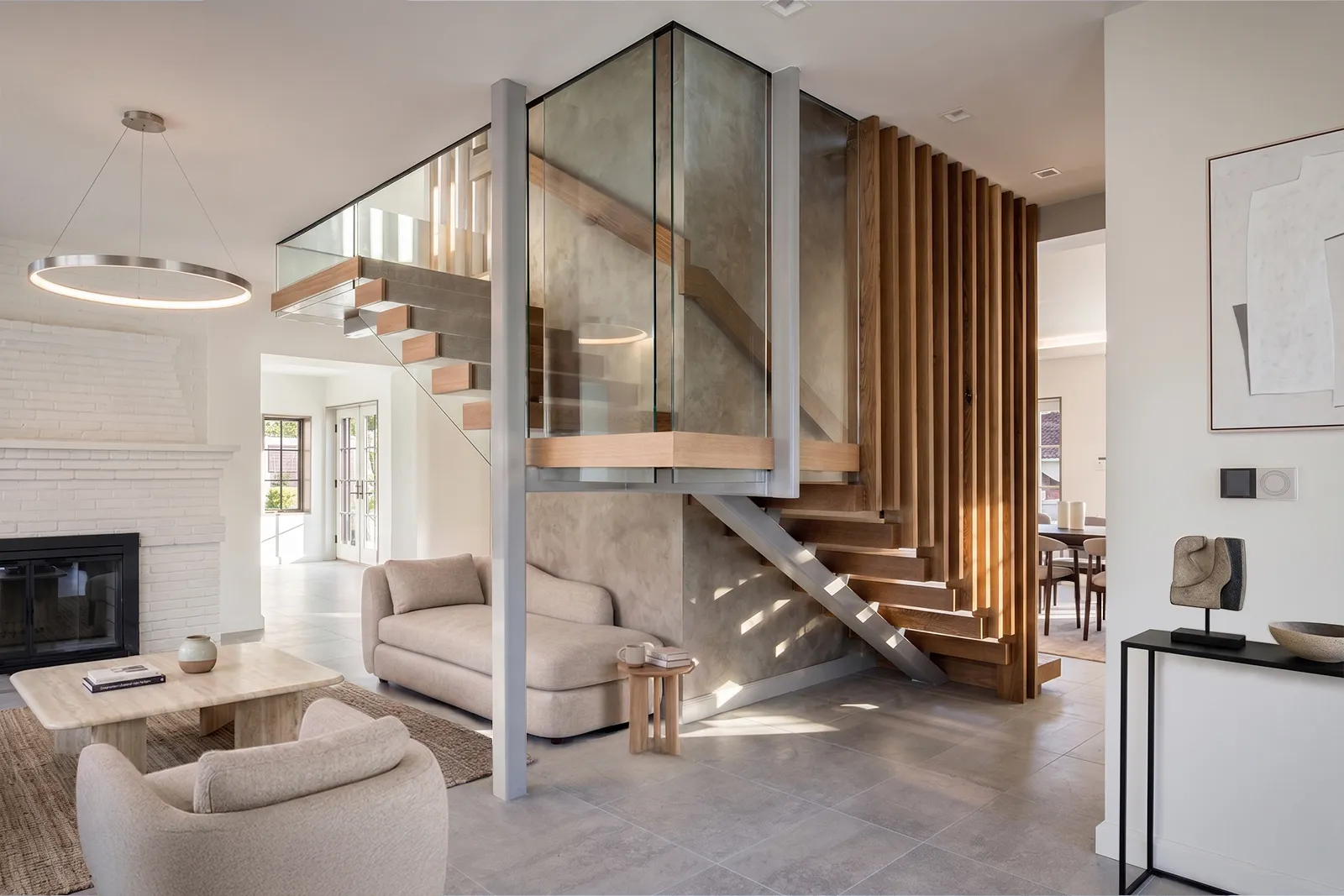 Long Island living room with a floating wood stair, glass railing, and a white-painted brick fireplace in a multigenerational home