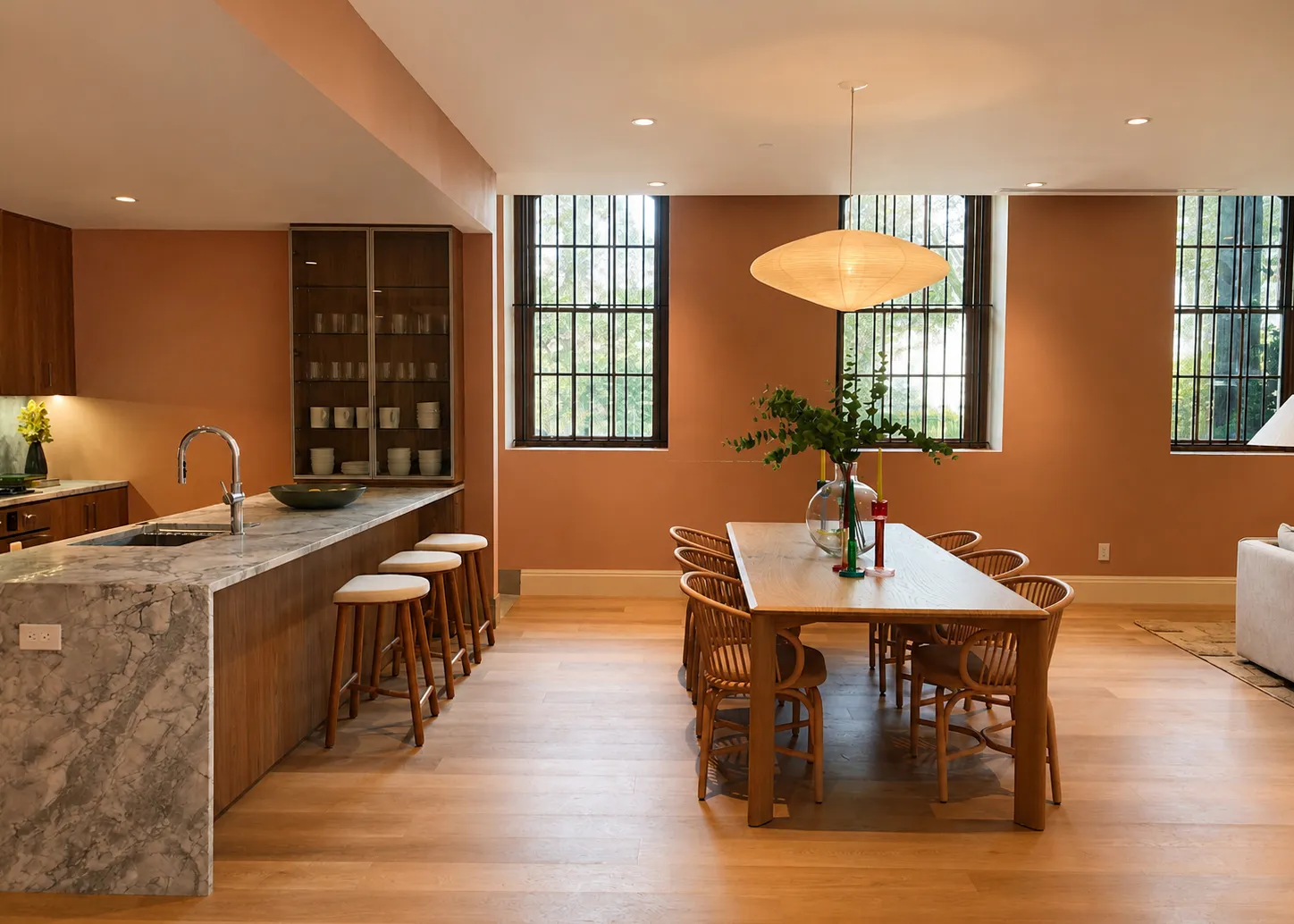 Open kitchen and dining room with terracotta walls, a marble waterfall island, and tall windows in an Astoria condo