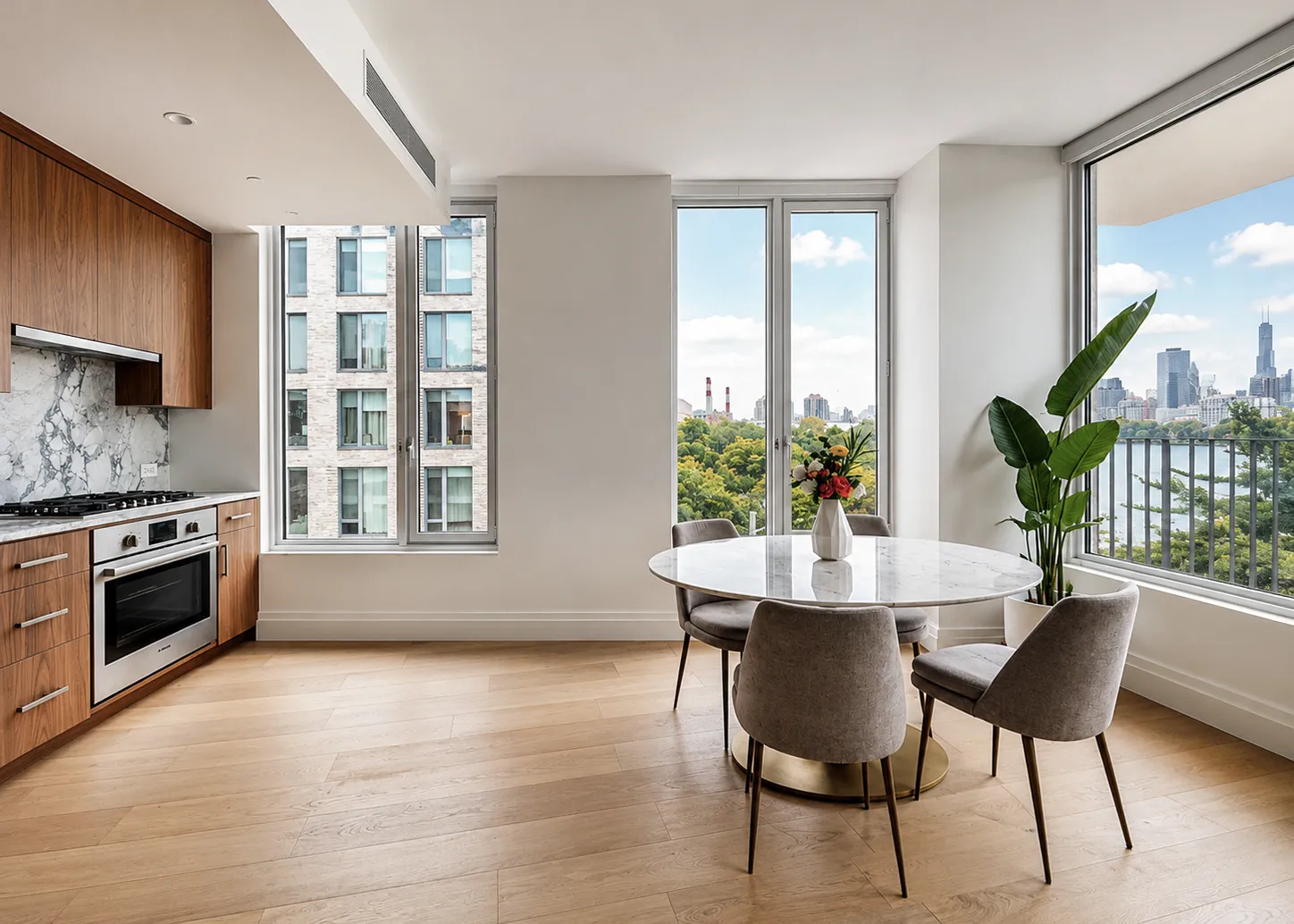 Astoria condo dining area with walnut kitchen, round marble table, and oak floors beside windows with city and river views