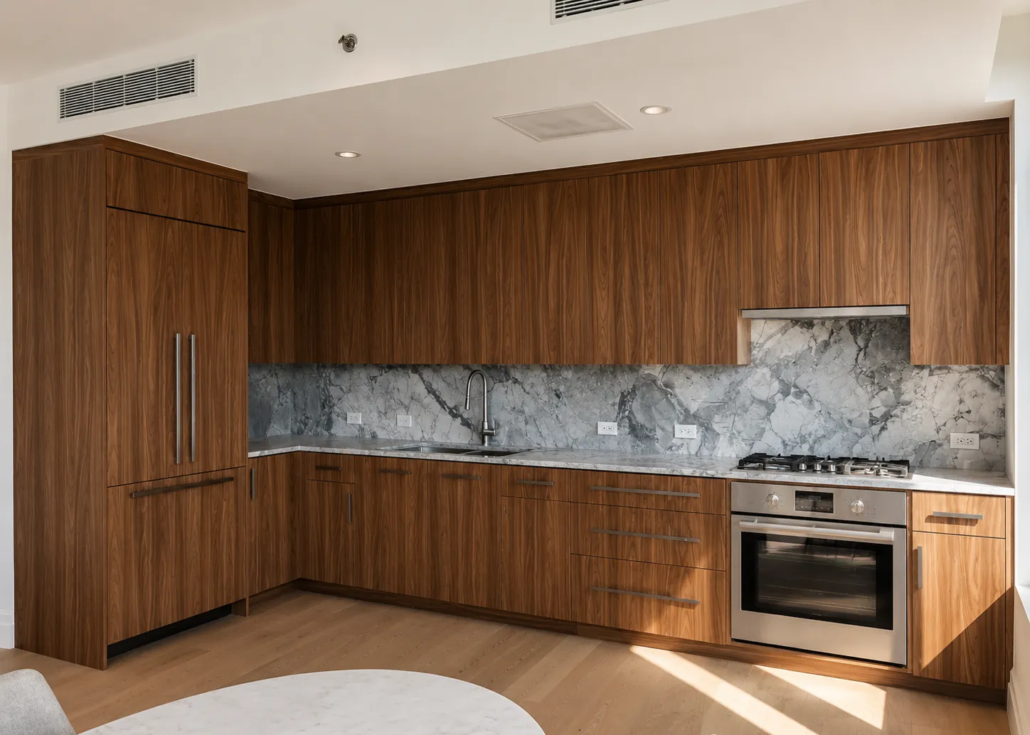 Condo kitchen with walnut cabinetry, marble backsplash, and stainless appliances in an Astoria mixed-use building