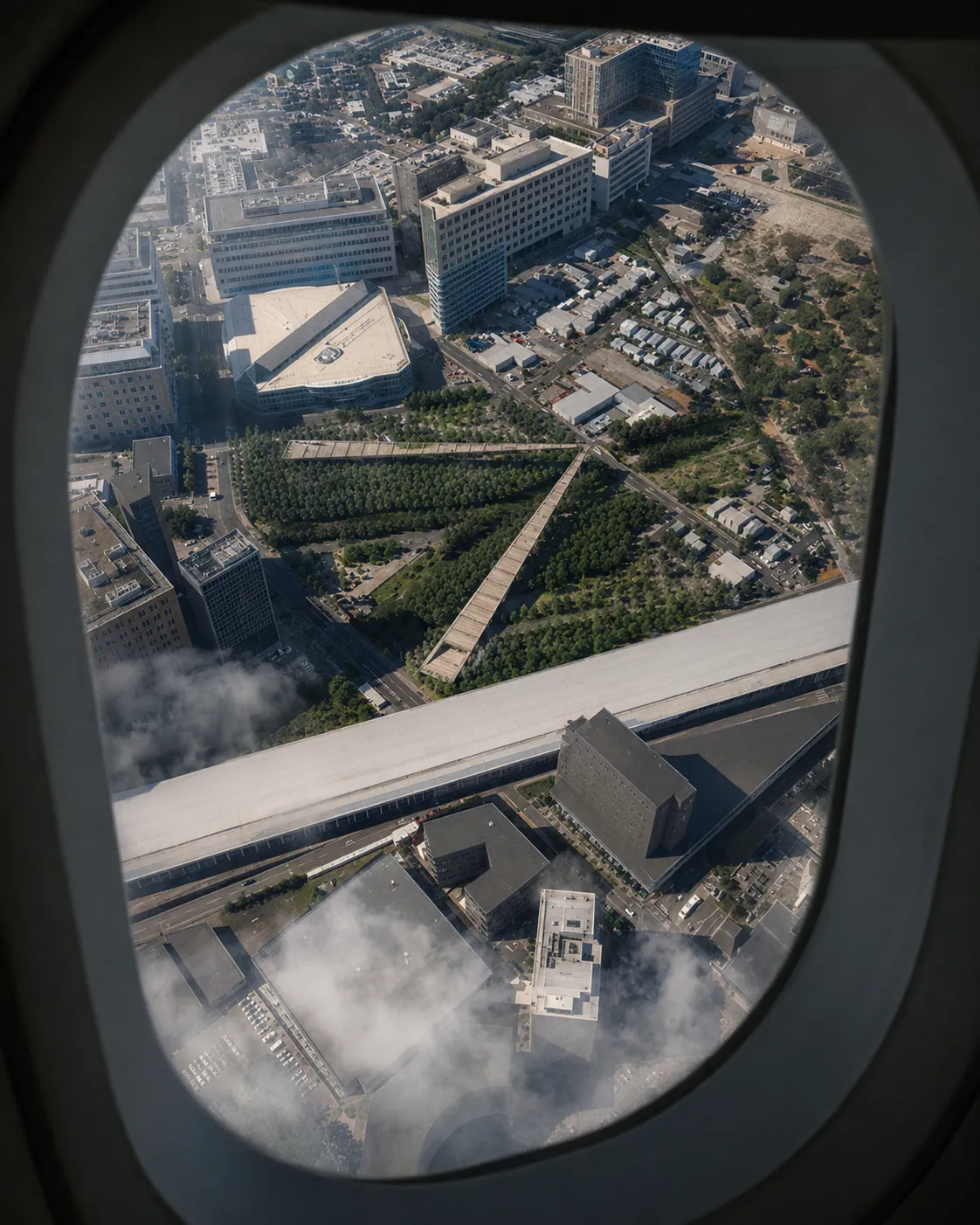 Aerial view through an airplane window of the angled walkway threading a wooded San Jose park between city blocks and a highway