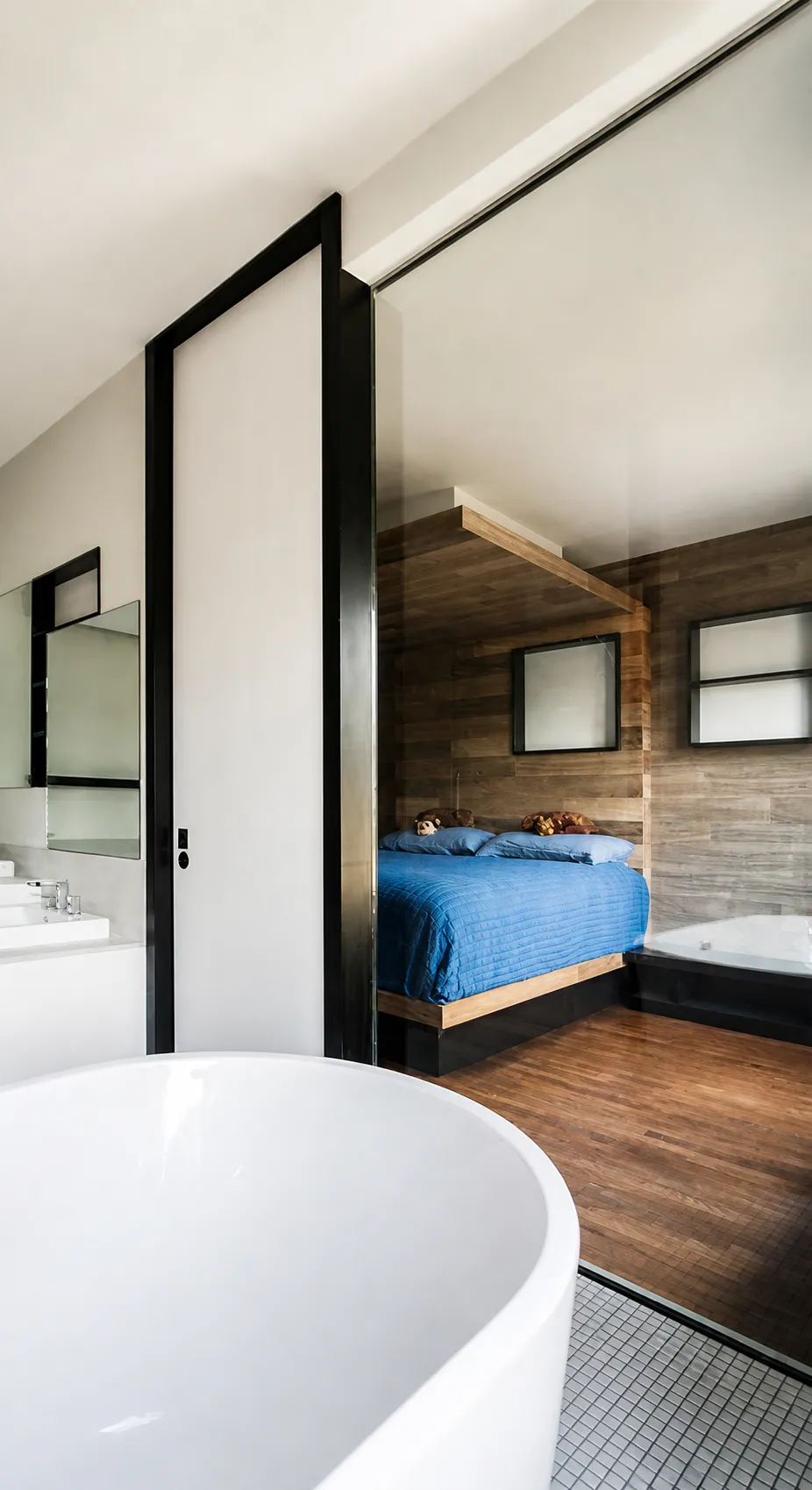 View through a glass partition from the master bath to the wood-wrapped canopy bed in a Manhattan suite