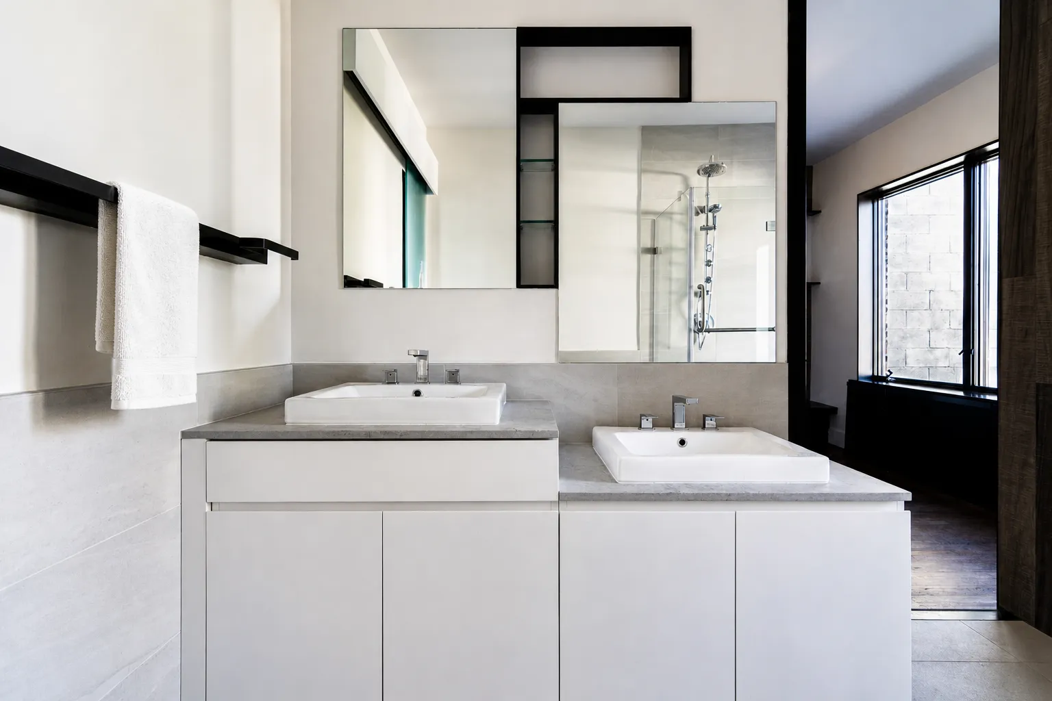 His-and-hers vanities set at two different heights in a Manhattan master bathroom, with stone tops and black-framed mirrors