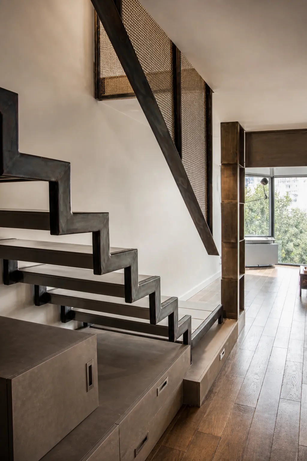  Sculptural brass box-shelving column with mixed metal finishes next to a polished steel stair in an Upper West Side duplex