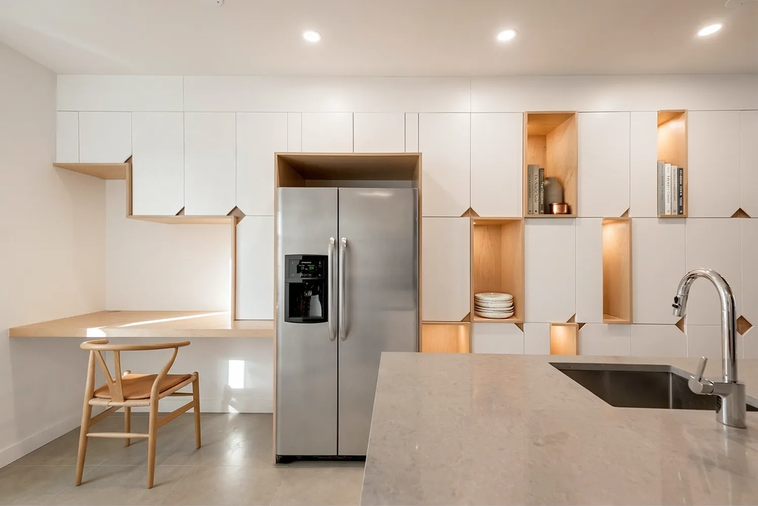 Brooklyn kitchen with a wall of white cabinetry and warm wood-lined display niches, a built-in desk nook, and a stone island