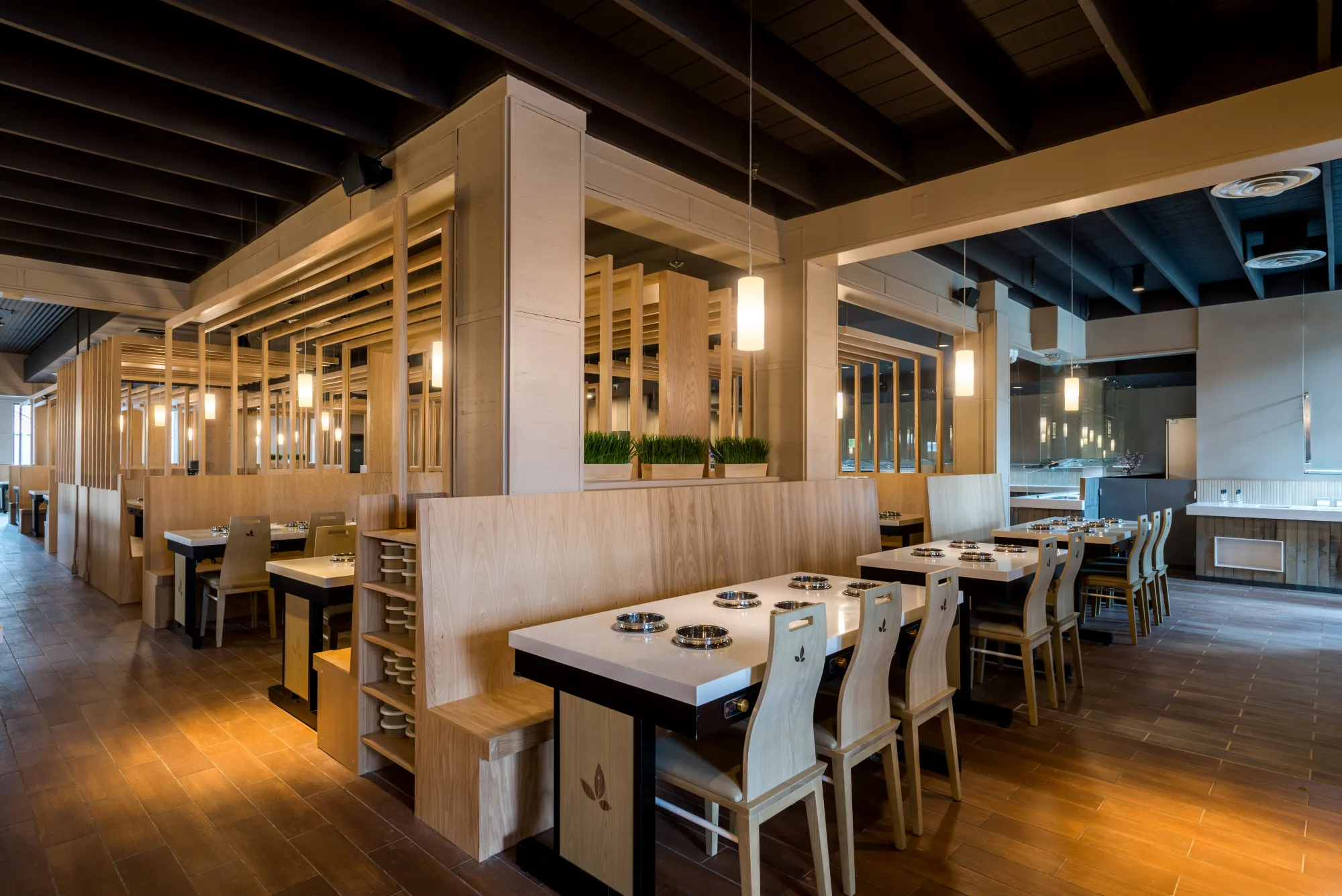 Rows of booth-style hot pot tables divided by wood-slat screens and mirrored columns in a restaurant interior