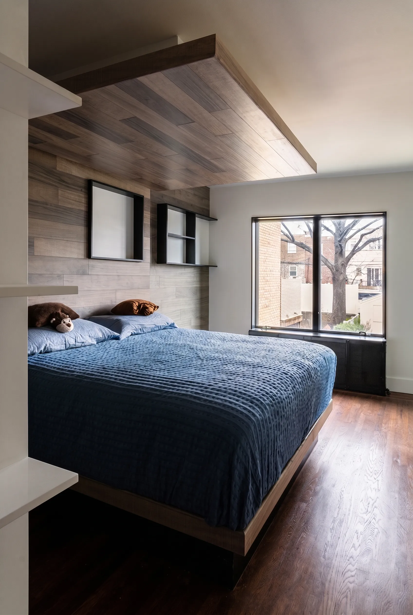 Manhattan master suite bedroom with a sculptural wood canopy over the bed and a black-framed window looking onto bare trees