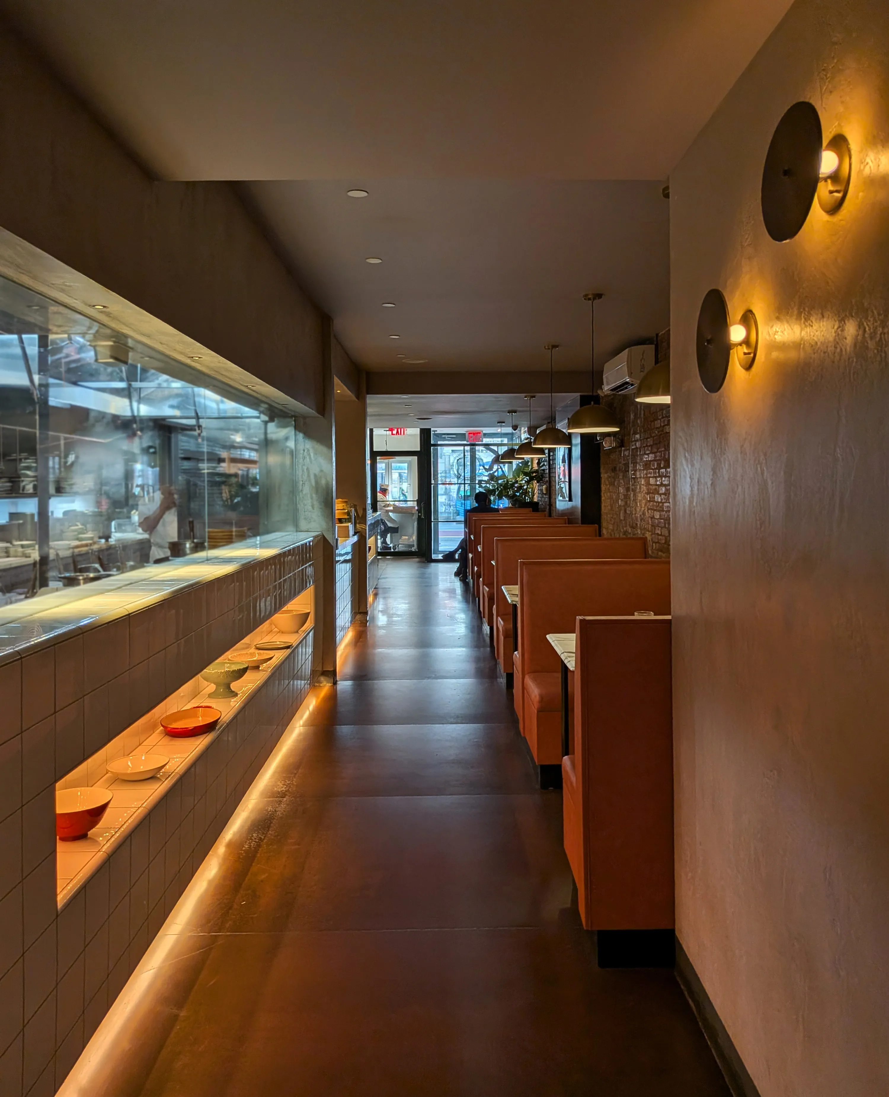 Dining corridor with leather banquettes facing an open kitchen behind glass in Chelsea, New York
