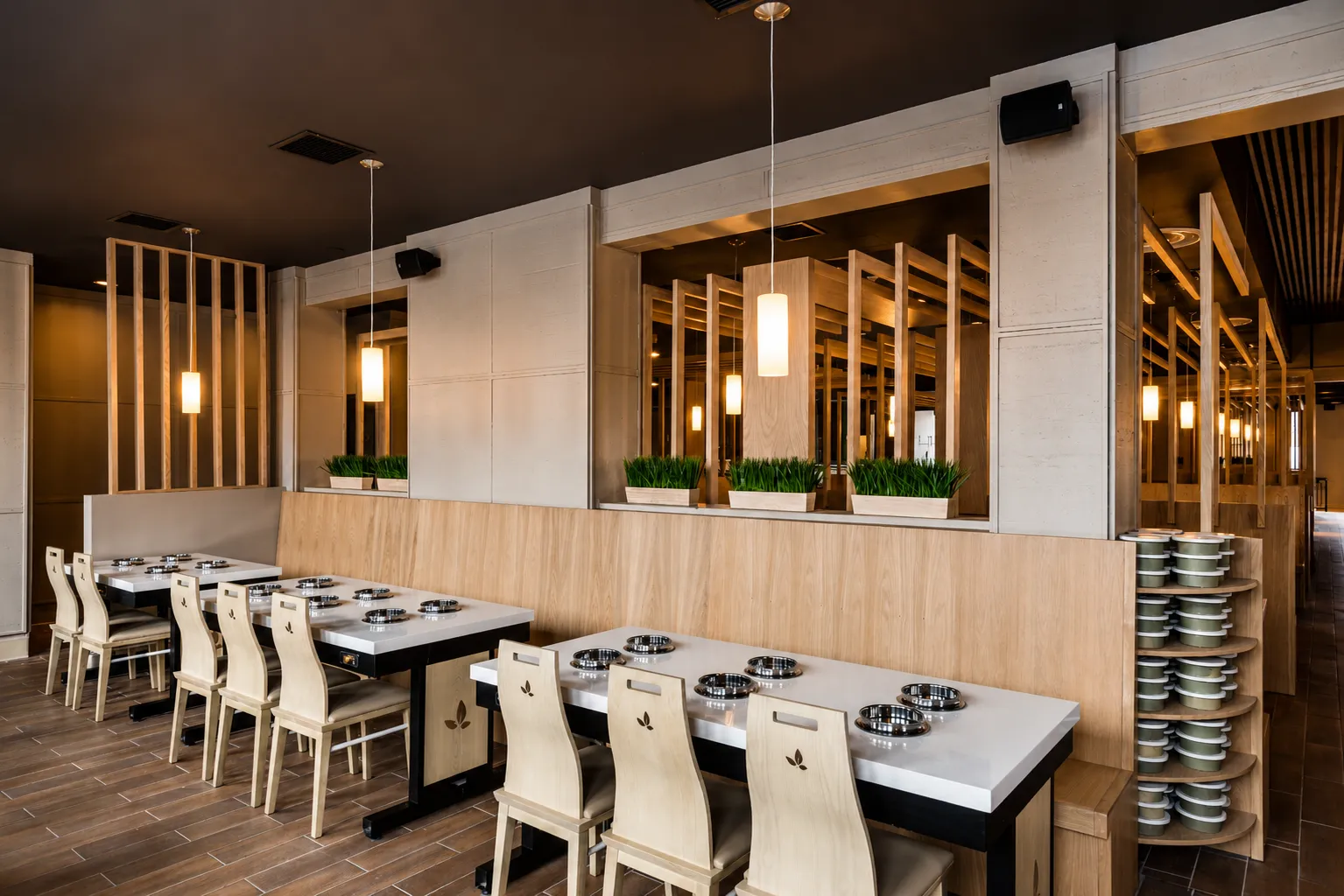 Hot pot dining tables with light-wood chairs and induction burners beside mirrored columns with planters
