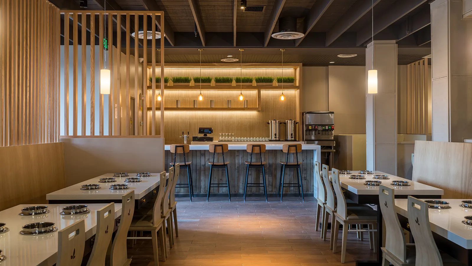 Hot pot restaurant dining room with individual induction-well tables, wood-slat partitions, and a reclaimed-wood service bar