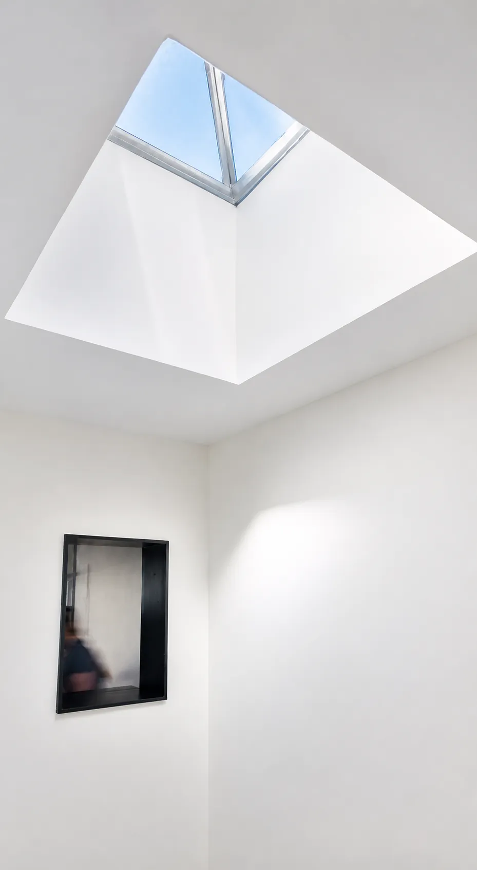 Pyramidal skylight well drawing daylight into a Manhattan master suite above a black-framed mirrored niche