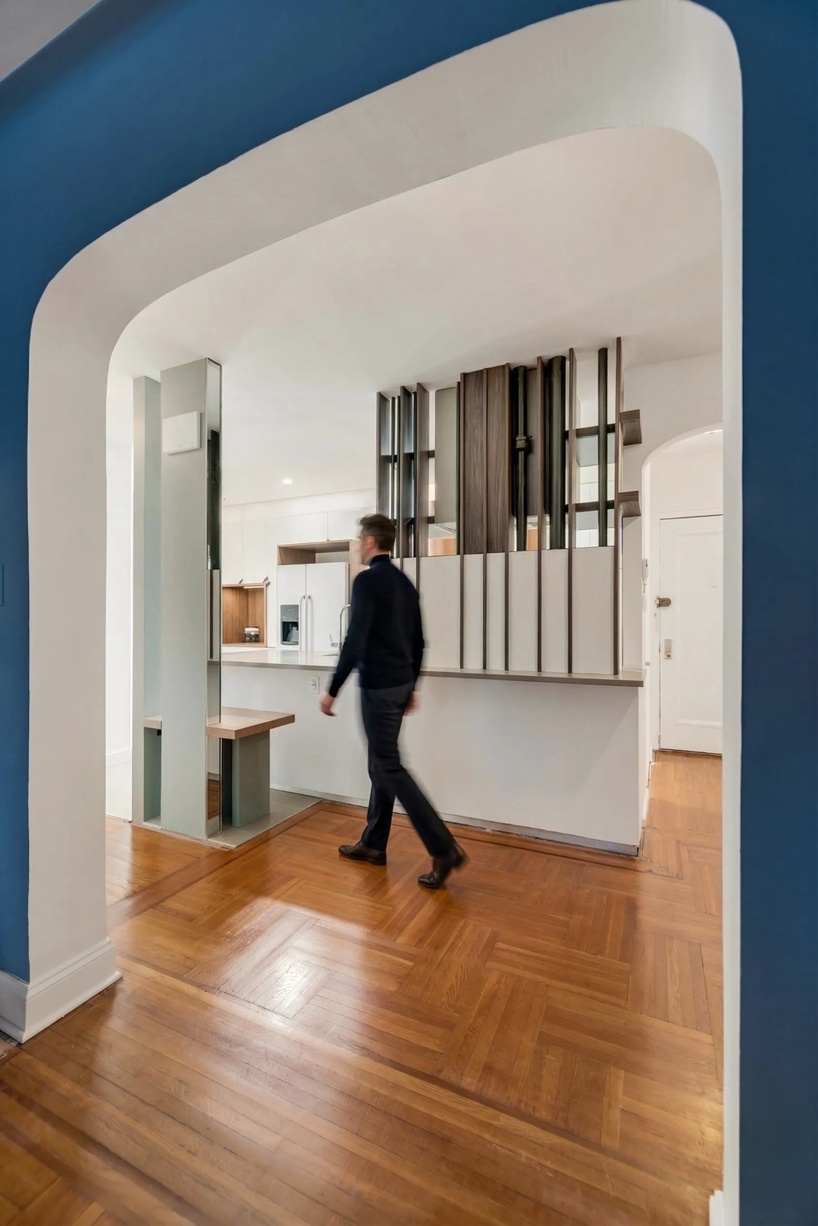 Deep blue arched openings framing a renovated Brooklyn kitchen, with a wood-slat screen over the peninsula and herringbone floors