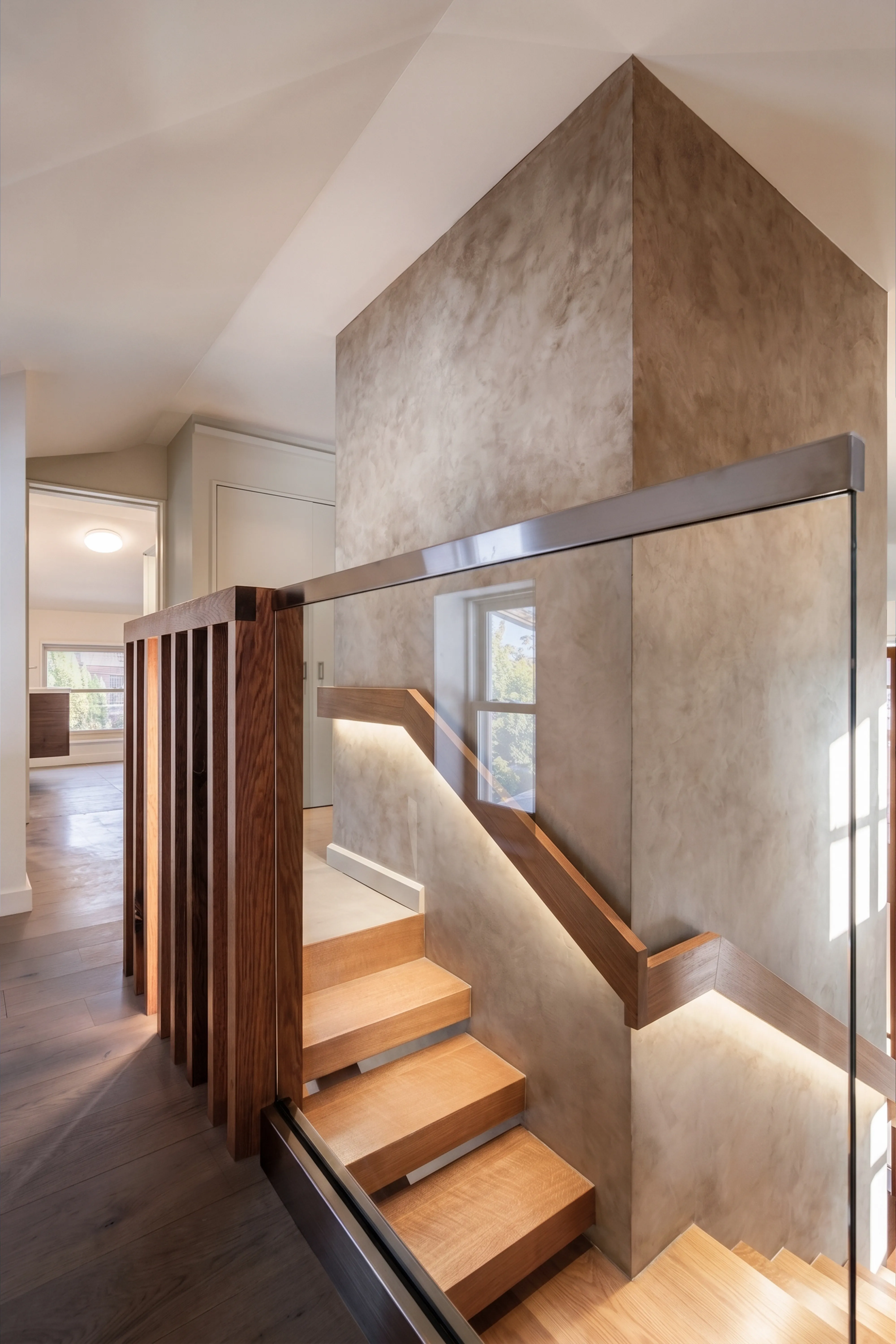 Stair landing with a plaster-clad core, glass railing, and wood-slat screen in a multigenerational Long Island home