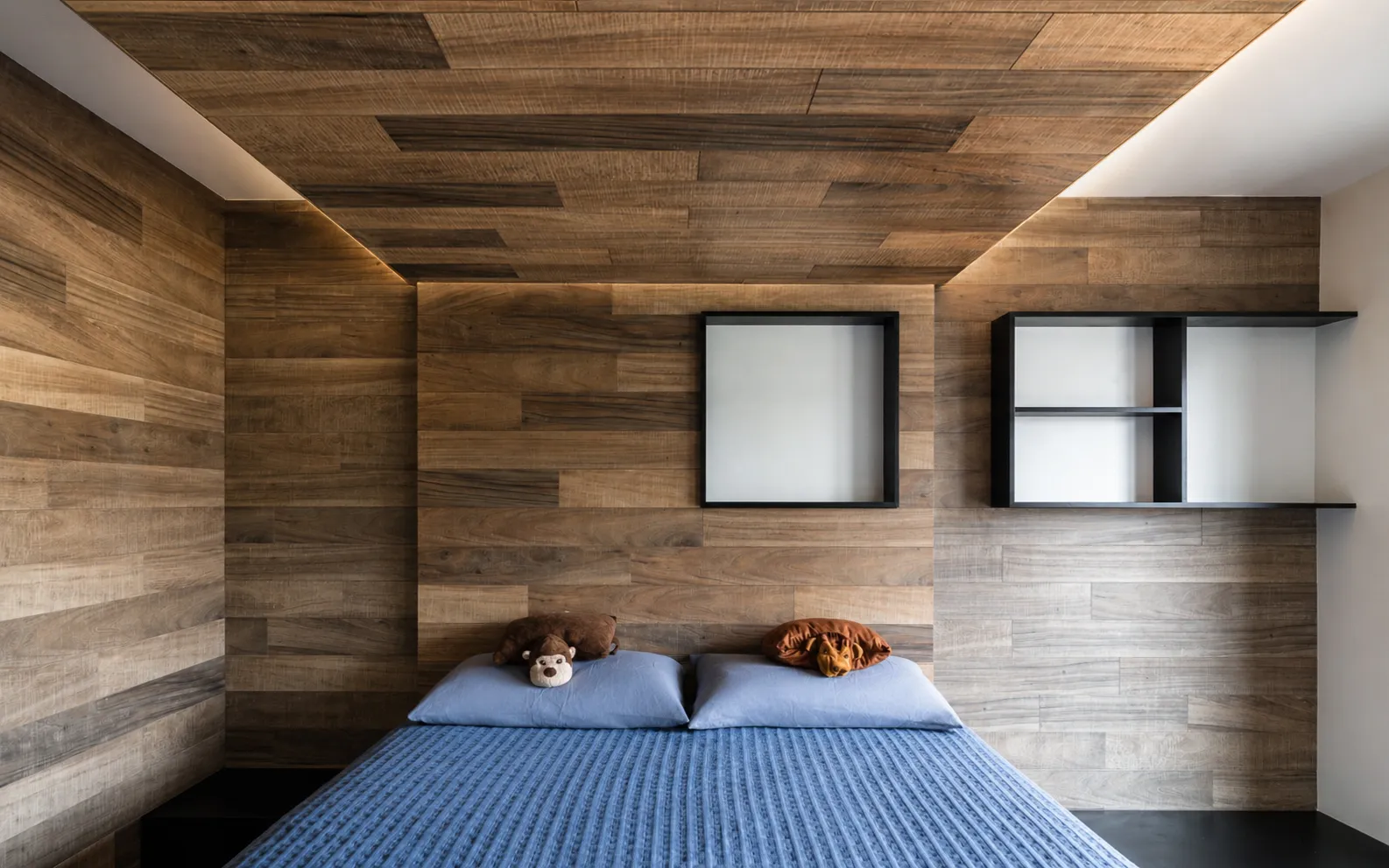 Wood-wrapped bedroom in a Manhattan master suite with a plank ceiling, black-framed niche shelves, and a blue knit bedspread